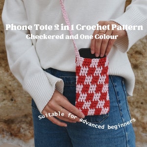 Puede incluir: Un bolso de teléfono de ganchillo a cuadros rojos y rosas con una correa rosa. El bolso está diseñado para guardar un teléfono y lo sostiene una persona que lleva vaqueros azules. El texto de la imagen dice "Phone Tote 2 in 1 Crochet Pattern Checkered and One Colour".