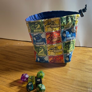 May include: A blue drawstring bag with a colorful stained glass pattern featuring the Hogwarts house crests. The bag is filled with multi-colored dice.