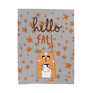 Könnte beinhalten: Eine graue Kuscheldecke mit einer niedlichen Illustration eines orangefarbenen Katers, der eine Tasse Kaffee hält. Die Decke hat ein sich wiederholendes Muster aus orangefarbenen Ahornblättern und den Text "hello fall" in Schwarz.