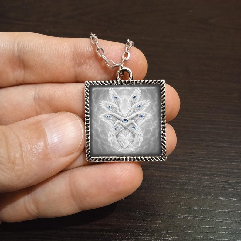 May include: Square pendant necklace with a silver chain. The pendant features a detailed illustration of a white, winged creature with multiple blue eyes against a gray background. The pendant is framed with a decorative silver border.