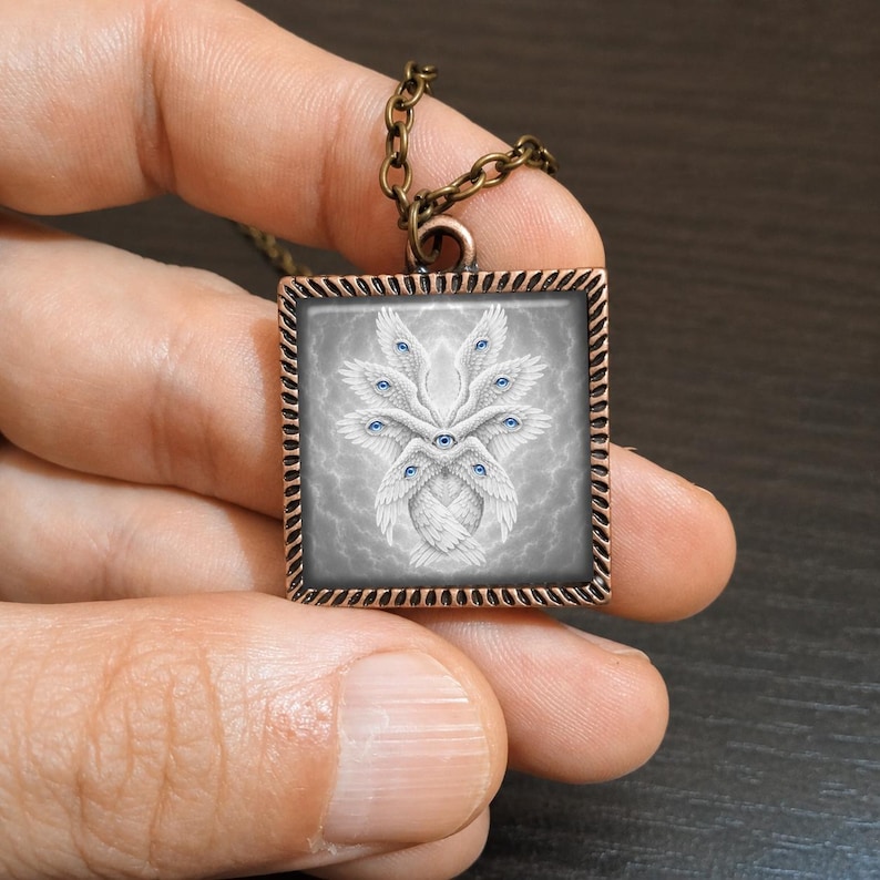 May include: Square pendant necklace with a bronze chain. The pendant features a detailed illustration of a white, winged creature with multiple blue eyes against a gray background. The pendant has a decorative border.