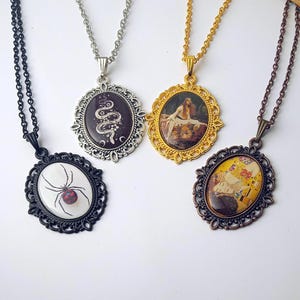 May include: Four ornate pendant necklaces with different designs. One features a spider, another a snake, and two others feature paintings. The pendants have oval frames and are suspended from chains. The colors include black, silver, gold, and bronze.