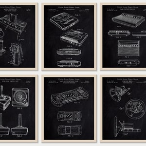 Op de afbeelding: Zes ingelijste patentprints van vintage videogamecontrollers en -consoles op een schoolbordachtergrond. De prints zijn in zwart-wit en tonen gedetailleerde technische tekeningen van de apparaten. De frames zijn neutraal van kleur.