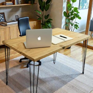 May include: A home office scene with a light wood desk on metal hairpin legs, a laptop, and a notebook. The desk rests on a neutral rug. A wooden cabinet and shelves with decor are in the background. The desk is approximately 120 cm long.