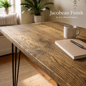 May include: A rectangular wooden desk with a dark brown Jacobean finish and black metal hairpin legs. The surface features visible wood grain and knots. A beige ceramic mug, a closed notebook, and a black pen rest on the desk surface.