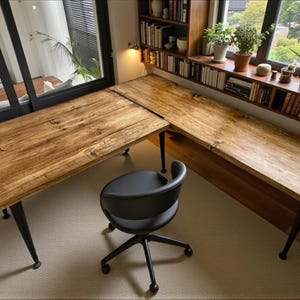 May include: An L-shaped wooden desk with a natural grain finish and black metal legs, paired with a black swivel office chair featuring a curved backrest. The desk surface is smooth and rectangular, providing a workspace for home or office.