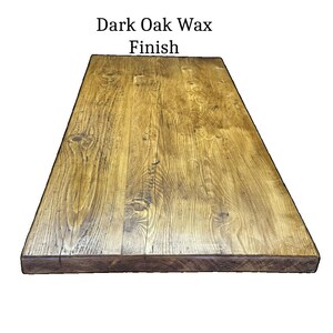May include: A rectangular wooden tabletop featuring a dark oak wax finish. The surface displays a prominent natural wood grain pattern with visible knots and variations in the brown wood tones. The text "Dark Oak Wax Finish" is centered above.