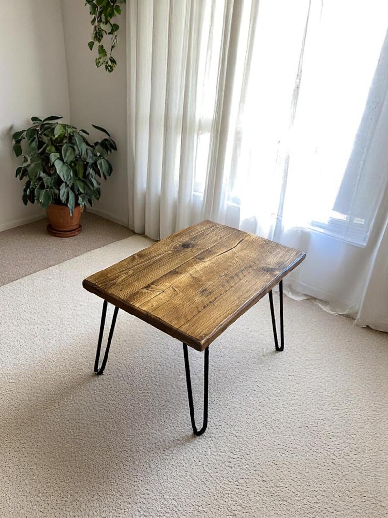 May include: A rectangular wooden coffee table with a natural finish. The table has black hairpin legs. The table is approximately 30 inches long, 18 inches wide, and 16 inches tall.