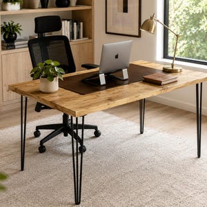 May include: A rectangular wooden desk with a natural grain finish and four black metal hairpin legs. The desk features a dark brown leather desk mat, a silver laptop on a stand, a small potted green plant, and a closed notebook on the surface.