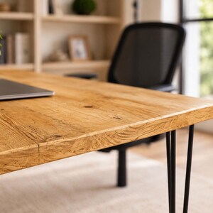 May include: A rectangular wooden desk featuring a natural light brown grain pattern and a smooth surface. The desk is supported by four thin, black metal hairpin legs. A small white ribbed planter with a green plant sits on the left side.