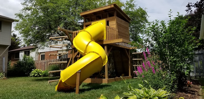May include: A yellow plastic slide attached to a wooden treehouse playset. The slide is curved and has a wooden platform at the top.