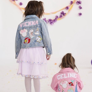 May include: Two children wearing denim and pink jackets with patches. The denim jacket has the name "VIENNA" on the back and Disney-themed patches. The pink jacket has the name "CELINE" on the back and Disney-themed patches. Both children are wearing skirts.