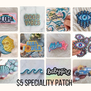 May include: Assortment of embroidered iron-on patches with various designs, including a sun and moon, a wave, a seashell, a car with sunflowers, a girl power patch, an eye with a star, a heart with the text "Live in the Sunshine", a flower with the text "Aloha", and a patch with the text "Good Vibes".