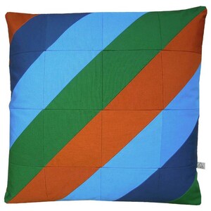 Könnte beinhalten: Quadratisches Zierkissen mit einem farbenfrohen diagonalen Streifenmuster. Das Design zeigt abwechselnde Streifen in Marineblau, Hellblau, Grün und Orange. Das Kissen hat ein gestepptes Aussehen mit aufgenähten Quadraten.