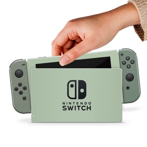 May include: A sage green Nintendo Switch console with a matching Joy-Con controller. The console is open and the screen is visible. The Nintendo Switch logo is on the front of the console.