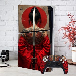 May include: A PlayStation 5 console with a custom skin depicting a woman with tattoos, a sword, and a red sun. The matching controller has a similar design. The console is set against a white brick wall.