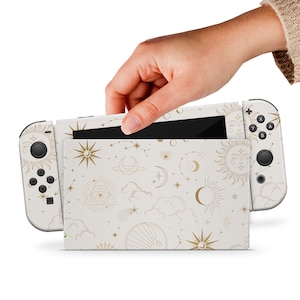 Pode incluir: Console Nintendo Switch branca com uma pele de design celestial dourado e branco. A pele apresenta um padrão repetitivo de luas, estrelas, sóis e nuvens.