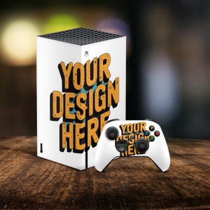 Könnte beinhalten: Eine weiße Spielkonsole und ein Controller mit dem Text "YOUR DESIGN HERE" in Orange und Schwarz. Die Konsole hat eine schwarze Oberseite mit einem Gittermuster. Der Controller ist weiß mit schwarzen Knöpfen und farbigen Akzenten.