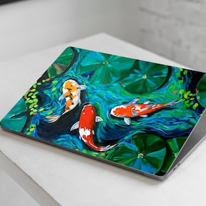 Può includere: Un laptop con un design colorato che presenta tre pesci koi che nuotano in uno stagno con ninfee. I pesci sono arancioni, bianchi e neri.