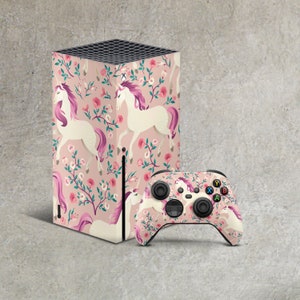 May include: A pink and white gaming console skin with a floral pattern and unicorns. The skin is designed for the Xbox Series X console. A matching pink and white controller skin with the same pattern is also shown.