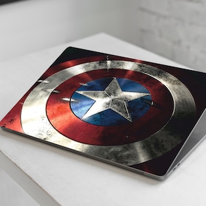 May include: A laptop with a distressed, red, white, and blue Captain America shield design on the lid.