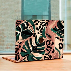 May include: A laptop computer with a colorful tropical-themed design featuring green leaves, pink and brown leopard print, and gold accents.