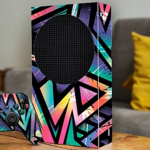 May include: A black and white gaming console with a colorful geometric design. The console has a black speaker grill and a matching controller with the same design.