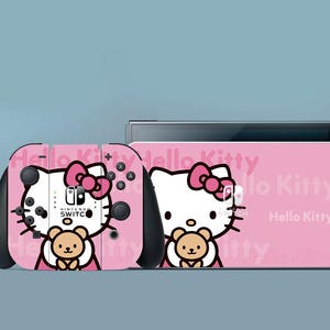 Può includere: Console e controller Nintendo Switch rosa con design Hello Kitty e orsetto. I controller hanno dettagli neri e la console riporta la scritta "Hello Kitty".