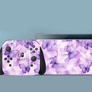 May include: A Nintendo Switch console and controllers with a purple butterfly design. The controllers and console have a light purple background with purple butterflies. The text "NINTENDO SWITCH" is visible on the controller.