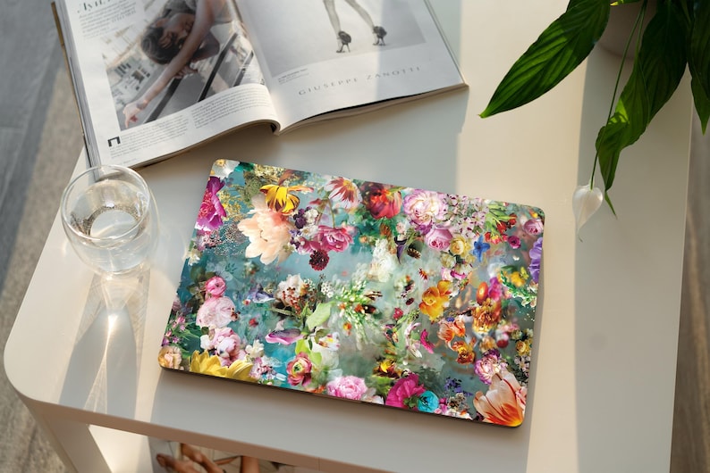 K&ouml;nnte beinhalten: Eine Laptop-Haut mit einem farbenfrohen Blumendesign. Das Design zeigt eine Vielzahl von Blumen in den Farben Rosa, Lila, Gelb und Blau auf einem gr&uuml;nen Hintergrund. Die Blumen sind in einem zuf&auml;lligen Muster angeordnet, was ein lebendiges und auff&auml;lliges Design ergibt.