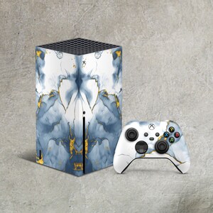 May include: A blue and gold marble-patterned skin for a gaming console and controller. The console is a rectangular box with a black front panel. The controller is white with black buttons and a black analog stick.