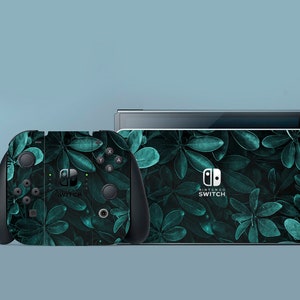 Può includere: Una console e un controller Nintendo Switch neri con un motivo a foglie verdi. La console ha il logo Nintendo Switch e il testo "NINTENDO SWITCH".