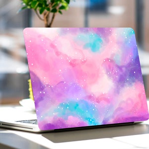 Könnte beinhalten: Ein Laptop mit einem pink-, lila- und blaufarbenen Galaxie-Design auf dem Deckel. Das Design zeigt weiße Sterne und einen Aquarell-Effekt.