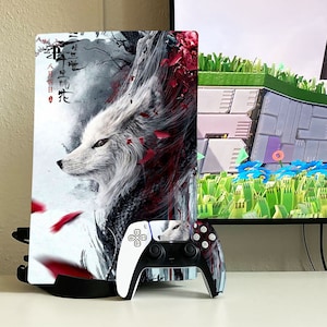 May include: A white and red video game console skin with a stylized image of a white fox with red accents. The console skin is on a black stand. A black and white video game controller with a white fox design is in front of the console.