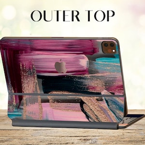 May include: A pink, blue, and gold abstract design iPad case with a black keyboard. The case has a brushed metal finish and a cutout for the camera lens. The keyboard is attached to the case with a magnetic hinge.
