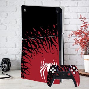 Könnte beinhalten: Eine schwarze und rote PlayStation 5 Konsole mit einem schwarzen und roten Spinnennetz-Design. Die Konsole steht neben einem schwarzen und roten PlayStation 5 Controller mit einem Spinnennetz-Design.