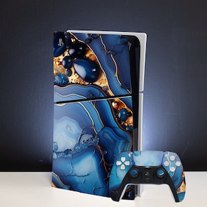 Könnte beinhalten: Eine blaue und goldene PlayStation 5 Konsole mit einer benutzerdefinierten Haut, die ein wirbelndes Achatmuster zeigt. Die Konsole wird mit einem passenden blauen und goldenen Controller geliefert.