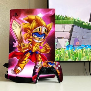 Puede incluir: Una consola PlayStation 5 rosa y dorada con una piel personalizada que presenta un personaje de dibujos animados con armadura dorada sosteniendo una espada. La consola está en un soporte negro y un mando a juego está delante de ella.