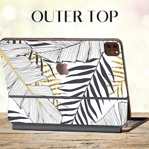 May include: A black and white iPad case with a tropical leaf design and gold glitter accents. The case has a cutout for the camera lens and the Apple logo. The case is shown on a wooden surface.