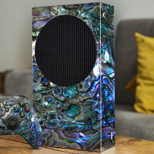 May include: A black and iridescent Xbox Series X console with a custom iridescent shell design. The console is sitting on a wooden surface next to a matching iridescent Xbox controller.