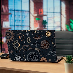May include: A laptop with a black cover featuring a celestial design of the sun, moon, stars, and clouds in gold and white. The laptop is on a wooden desk with a mouse and a small potted plant.