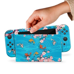 May include: A blue Nintendo Switch console skin with a design of koi fish swimming in a pond with cherry blossoms. The skin is designed to fit the Nintendo Switch console and Joy-Cons.