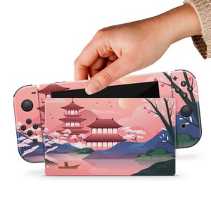 Op de afbeelding: Roze en blauwe Nintendo Switch console skin met een Japans geïnspireerd ontwerp met een pagode, kersenbloesems en een meer. De skin is ontworpen om te passen op de Nintendo Switch console en Joy-Cons.