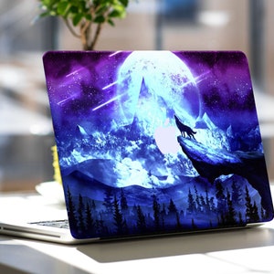 May include: Laptop skin featuring a wolf howling at the moon, set against a backdrop of a starry night sky. The design incorporates shades of blue, purple, and white, with a silhouette of a forest in the foreground. The laptop is silver.