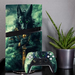 Può includere: Una console di gioco e un controller con un design di personaggio lupo verde e nero. La console ha una skin abbinata con la stessa grafica. Il controller ha pulsanti bianchi e una base nera. Una pianta di serpente in vaso è a destra.