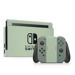 K&ouml;nnte beinhalten: Eine salbeigr&uuml;ne Nintendo Switch Konsolen-Dockingstation mit schwarzem Nintendo Switch Logo und Schriftzug, kombiniert mit einem passenden Controller-Griff. Der Controller hat schwarze Griffe, schwarze Tasten und ein mittiges salbeigr&uuml;nes Panel.