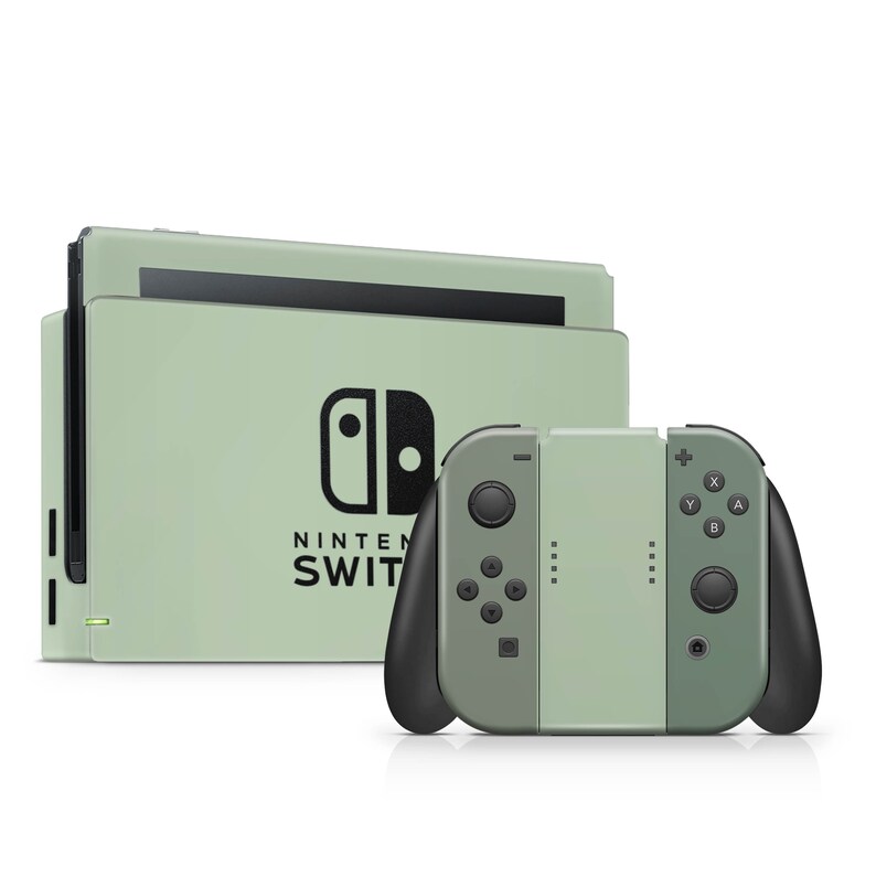 K&ouml;nnte beinhalten: Eine salbeigr&uuml;ne Nintendo Switch Konsolen-Dockingstation mit schwarzem Nintendo Switch Logo und Schriftzug, kombiniert mit einem passenden Controller-Griff. Der Controller hat schwarze Griffe, schwarze Tasten und ein mittiges salbeigr&uuml;nes Panel.