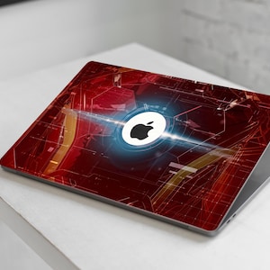 May include: A laptop with a red and gold design, featuring a glowing Apple logo. The design has a tech-inspired pattern with a bright blue light emanating from the logo. The laptop is on a white surface.