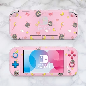 May include: Pink Nintendo Switch Lite console featuring a repeating pattern of a gray cat, bows, moons, stars, and hearts. The screen displays the Nintendo Switch logo. The console's buttons and controls are also pink.