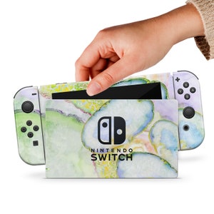 May include: A green, yellow, and purple watercolor design Nintendo Switch console skin with the Nintendo Switch logo. The skin is applied to the console and the Joy-Con controllers.